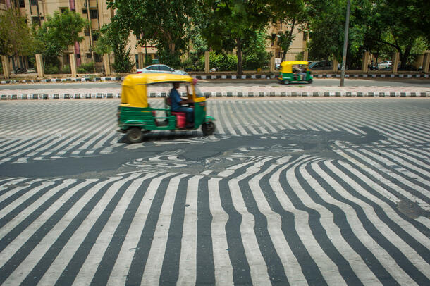 a tuk tuk drive over a walkway which lines are not straight because it melted