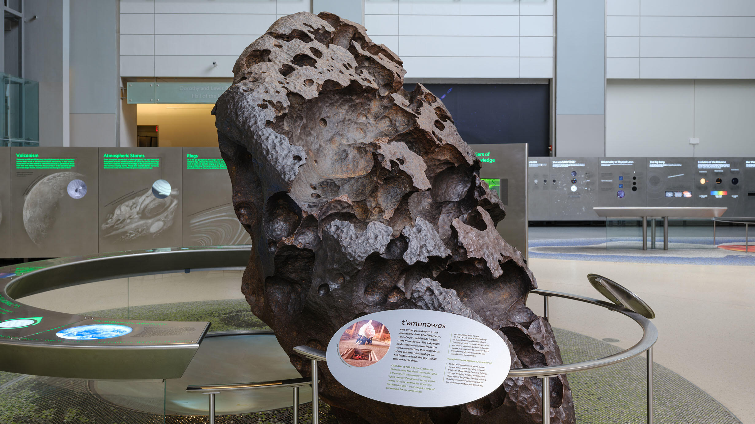 A large, pitted iron meteorite surrounded by a barrier with exhibit text describing its relationship to the Clackamas Chinook people.