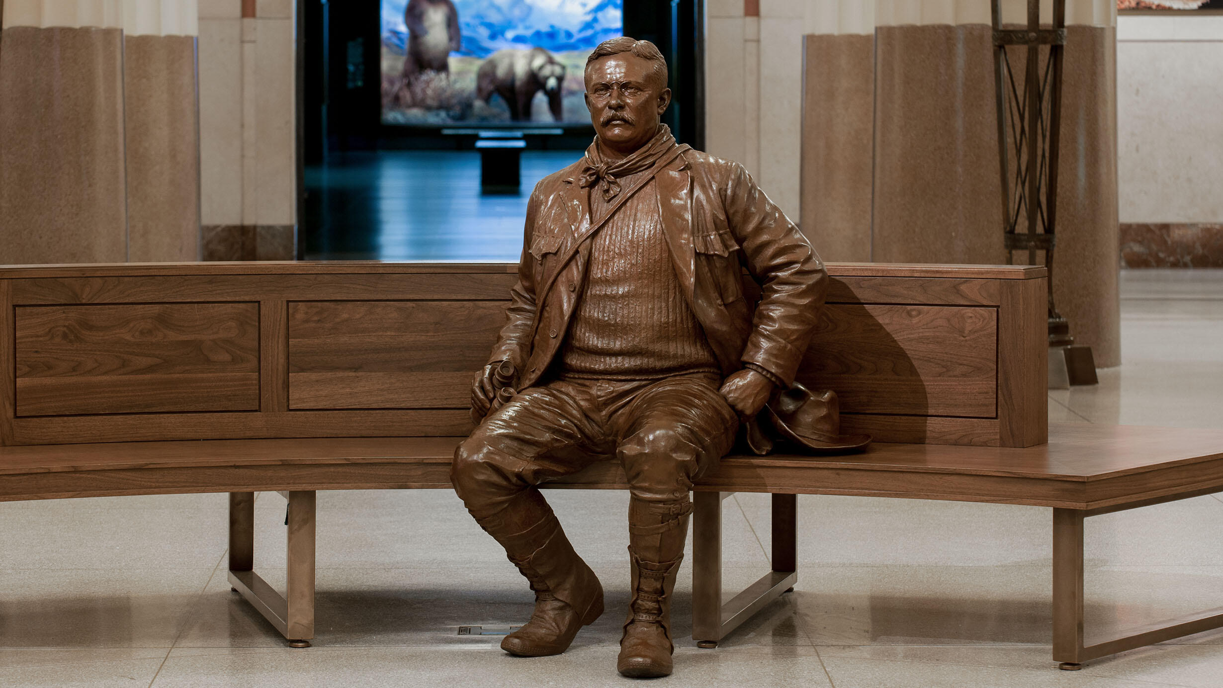 Bronze statue of Theodore Roosevelt appears to be seated on a wooden bench in the middle of the Museum's Theodore Roosevelt Memorial Hall.