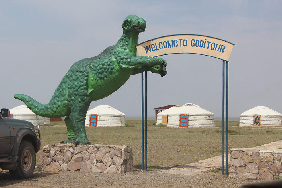 Bright green dinosaur statue next to a sign reading Welcome To Gobi Tour.