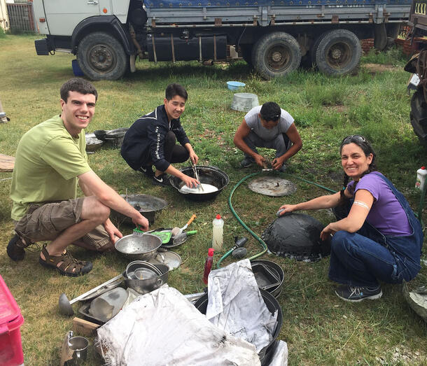 Four expedition members crouch on grass scrubbing kitchen pots and pans.