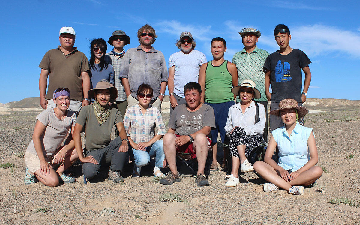 14 people pose in two rows in the desert.