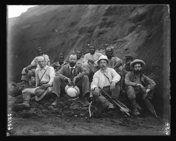 Ten people in two rows pose seated at the base of the volcano La Soufriere.
