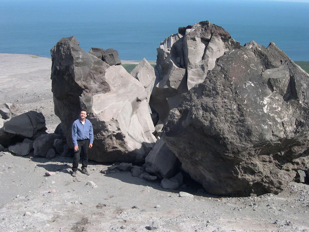 Man stands next to two enormous rocks, a volcanic boulder which has fallen and split in two.
