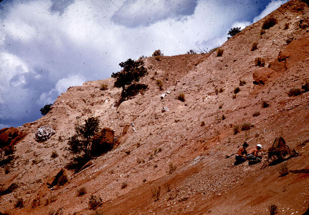 Two people working on a site on a sloping, rocky mountain. 