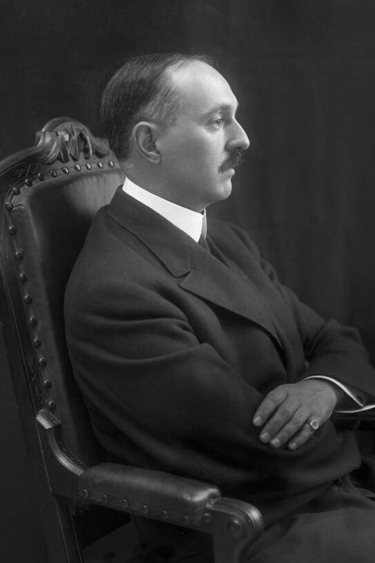 Man in a suit sits in a chair, shown in profile. 