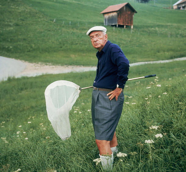 Vladimir Nabokov stands in a grassy field holding a butterfly net.