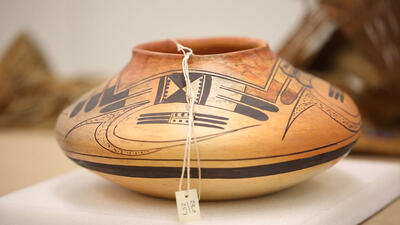 Round and low pot painted with geometric designs, with a paper label attached to the rim. 