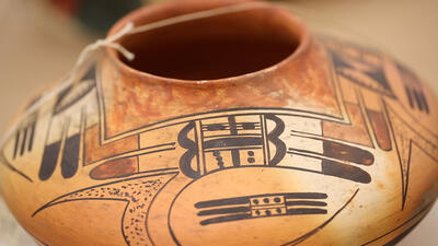 Round and low pot painted with geometric designs, with paper label attached to pot rim. 