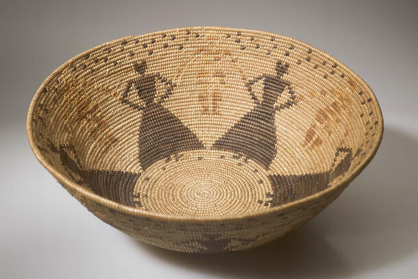 Woven basket with interior pattern of human figures wearing long dresses in darker color than the rest of the basket.