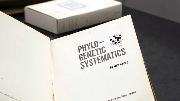 Book open to title page reading Phylo-Genetic Systematics by Willi Hennig and illustration of a clump of dark and light circles.
