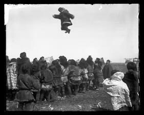 A person leaping in the air a few feet above a crowd of people huddled close together, using Walrus-Hide to toss person.