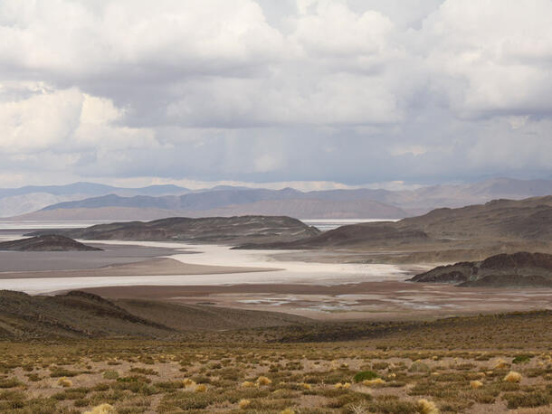 Landscape of low grassy hills in foreground and lake in the background surrounded by more hills. 