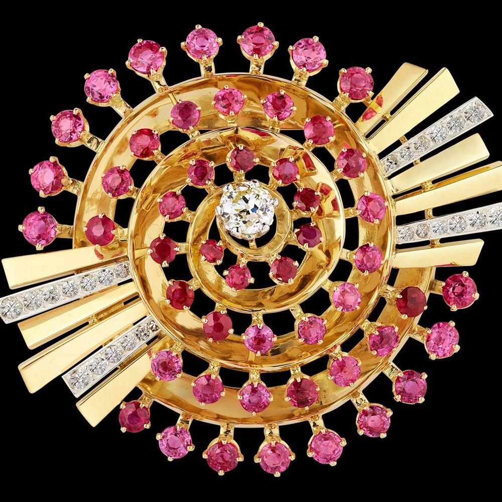 A bejeweled spiral clip studded with colorful rubies, a central diamond and ray-like pieces jutting out from two sides.