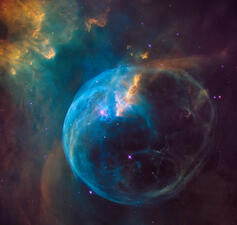 A bubble of colorful gas and dust in dark space, surrounded by bright speckled stars and light, cloud-like streaks.
