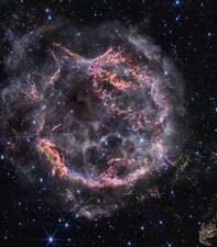 Brightly colored, wispy cloud-like shapes form a circular shape against dark space dotted with hundreds of bright stars.