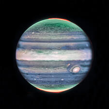 The planet Jupiter, with multicolored striped bands running across its surface, against a dark background.