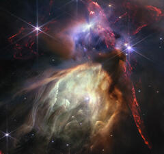 A large, bright, cloud-like mass shaped like a cave comes up against a tilted darker mass with three bright stars beaming around it.
