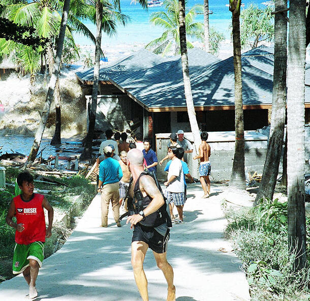 A group of people fleeing a tsunami crashing into a lodge with palm trees in the Andaman Islands, 2004