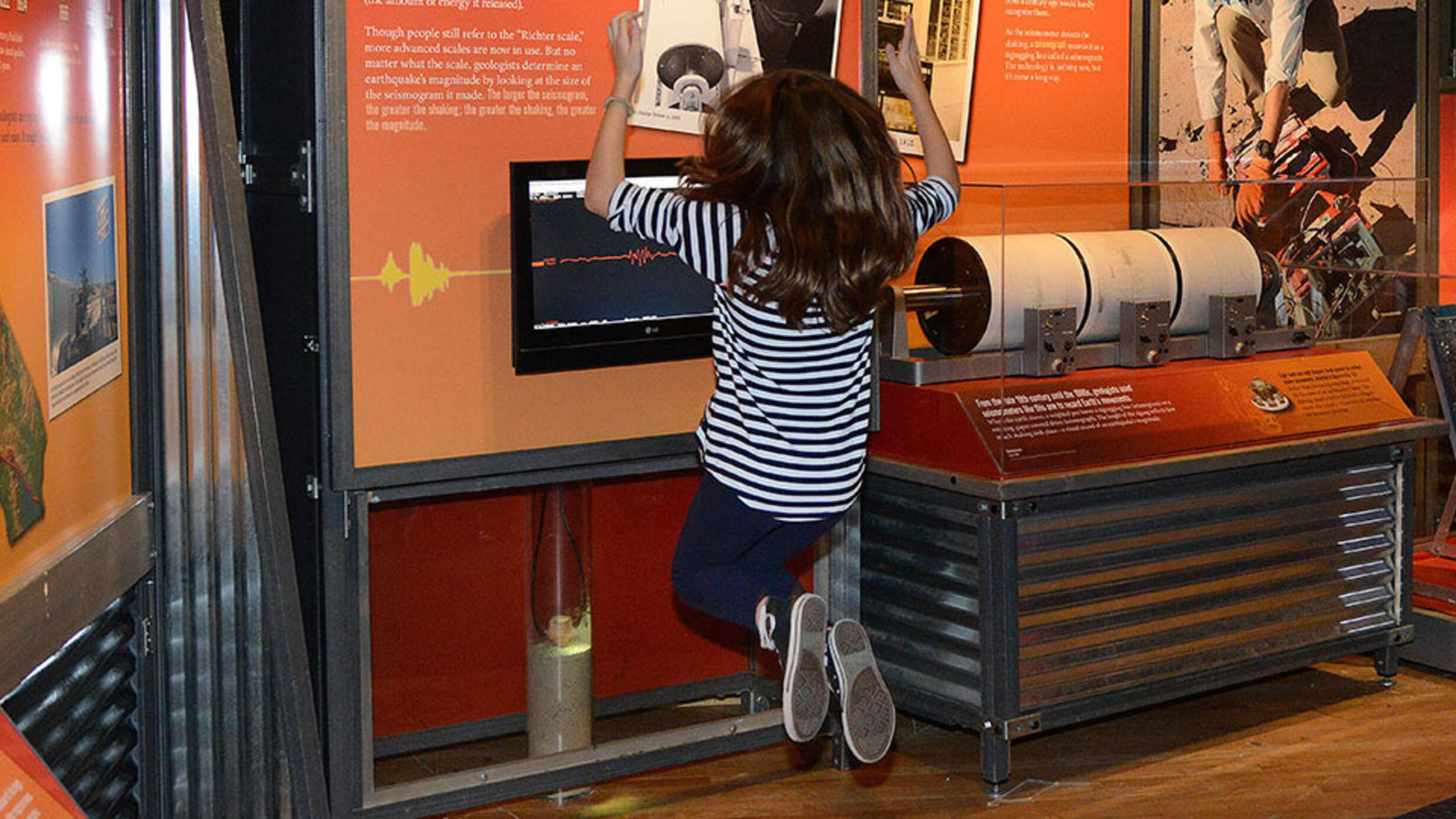 A child jumps on an interactive exhibit platform which demonstrates the Richter scale via a small screen surrounded by exhibit text.