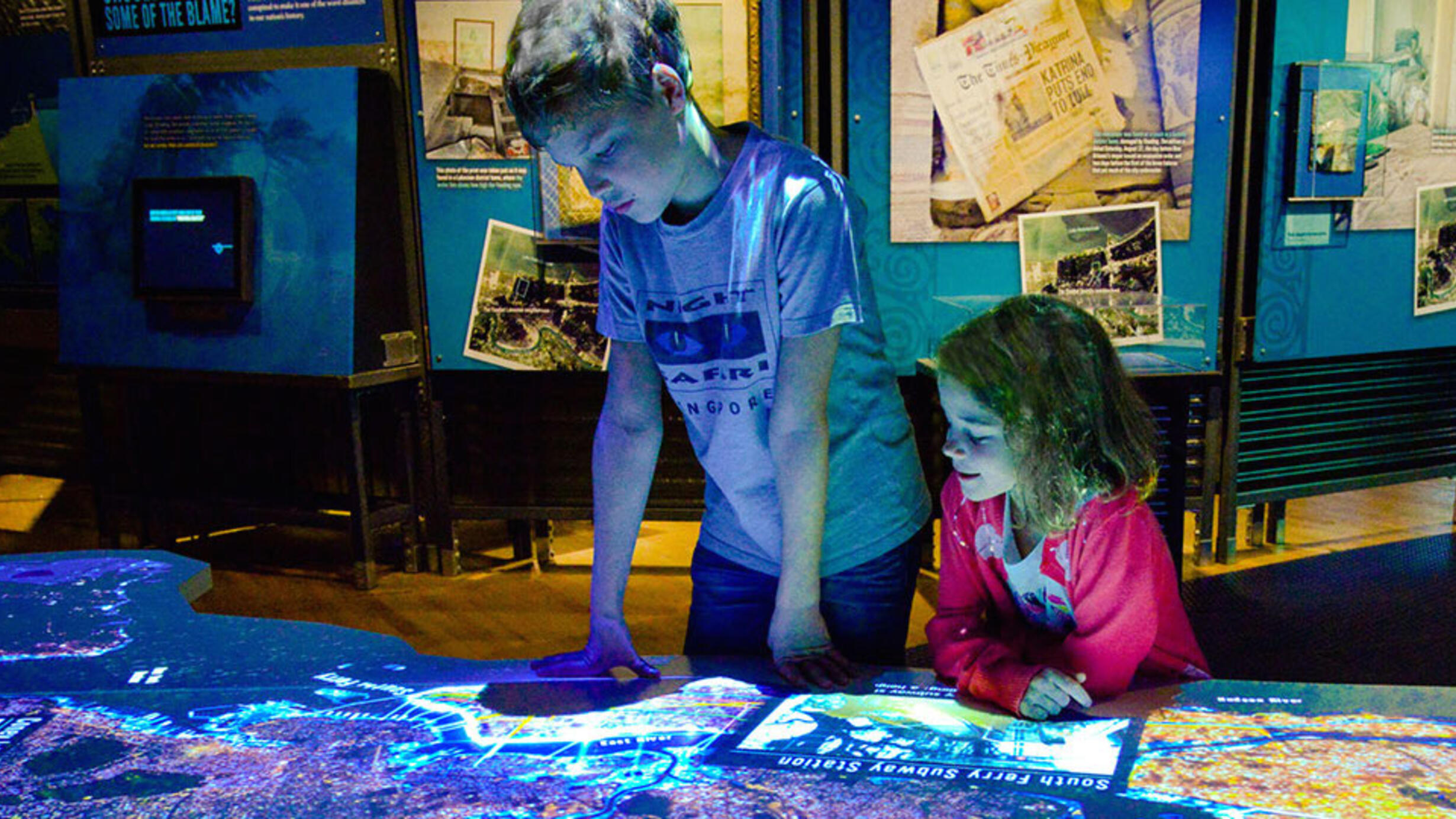 Two children lean on a digital display depicting a map of New York during Superstorm Sandy.