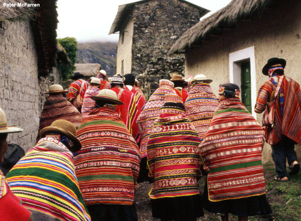 Bolivian villagers in bright woven shawls and ponchos walking through village