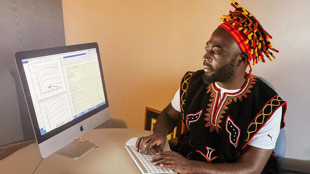 El científico Jude Kong se sienta a la mesa con las manos en un teclado, viendo una computadora de escritorio.