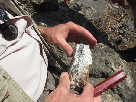 A medium-close outdoor shot of two hands holding a rectangular sample of rock.