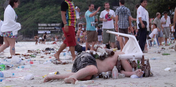 Tourist lying in trash on a beach sleeping off a night of drinking