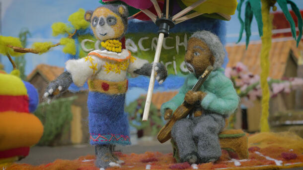 A felted Andean bear holds an umbrella and stands beside a seated Afro-Ecuadorian musician, also made of felt, who is playing a guitar.