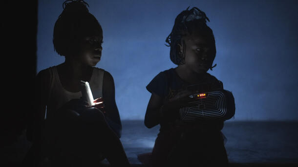 Two children sit in the dark holding objects with light that illuminate them. 