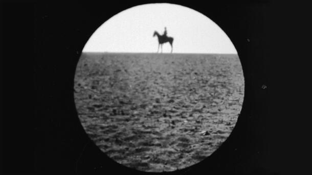 A person on a horse on a high horizon hazily visible in a circle as if through a camera lens.