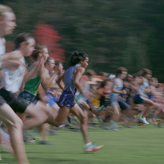 A blur of over 20 track runners in motion mid-race, with only Kutoven Stevens in focus running slightly ahead of the group in the foreground.
