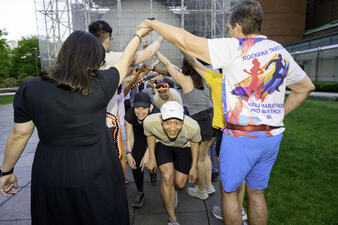 A line of runners crouch and run through a row created by two lines of people linking arms above to create an archway. 