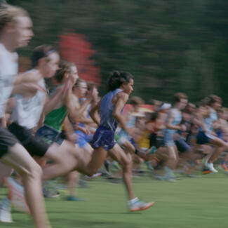 A blur of over 20 track runners in motion mid-race, with only Kutoven Stevens in focus running slightly ahead of the group in the foreground.