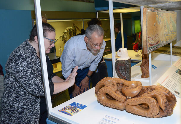 Two people examine a wood carving of an octopus and rat in an exhibit case.