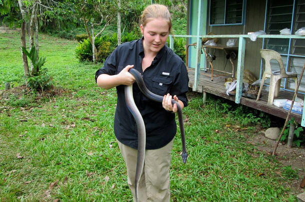 Oliver stands outside holding an approximately 7 foot long snake.