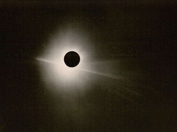 Rays of the sun are just visible behind the moon in a darkened sky.