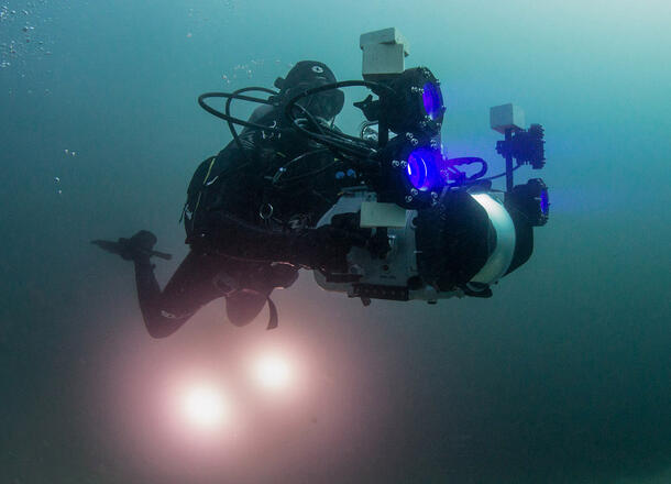 Scuba diver carries elaborate photo equipment as he swims underwater.