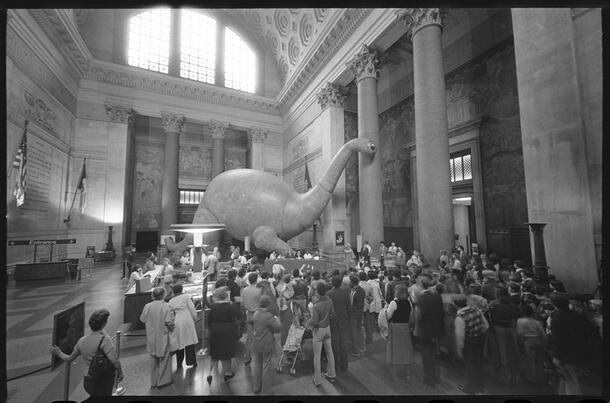 Large crowd stands around inflated dinosaur in the Museum's high-ceilinged rotunda.