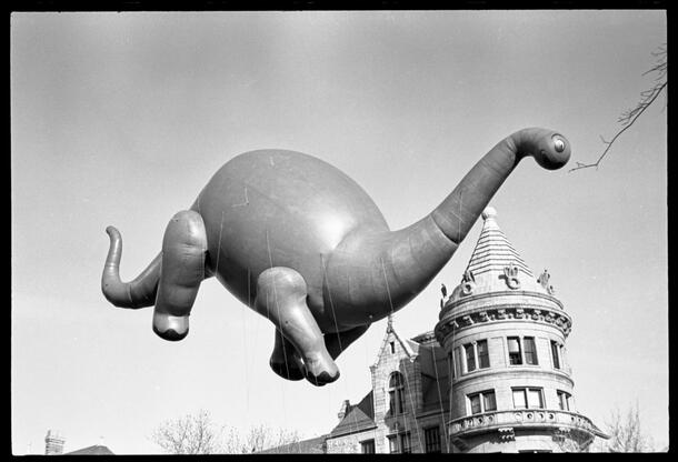 Dinosaur balloon floats in the air past one of the Museum's turrets.