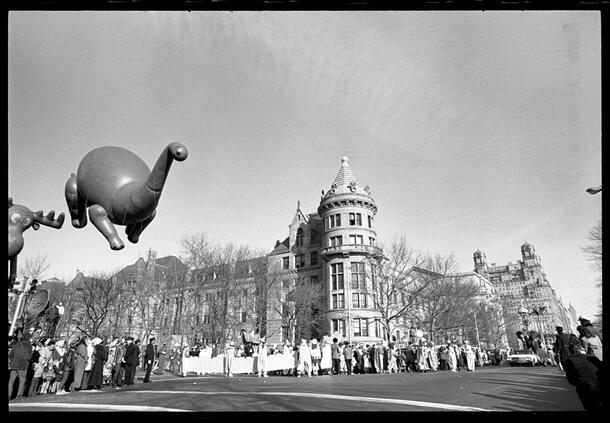 Dinosaur balloon floats along the street, with a full view of the Museum behind it.