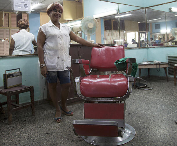 Mirta stands next to an old-fashioned style leather barber chair, with the mirrors of the salon in view behind her.