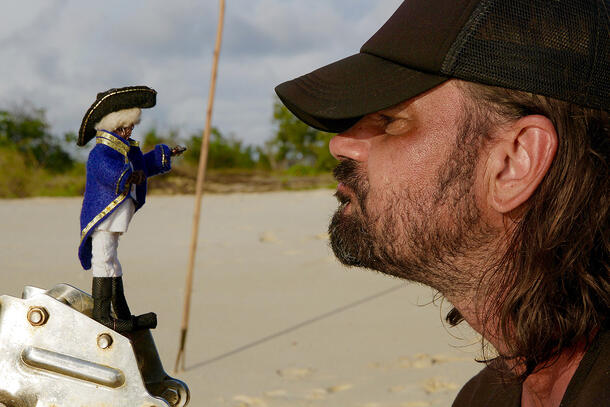 Man wearing a baseball cap looks at a Captain Cook doll.