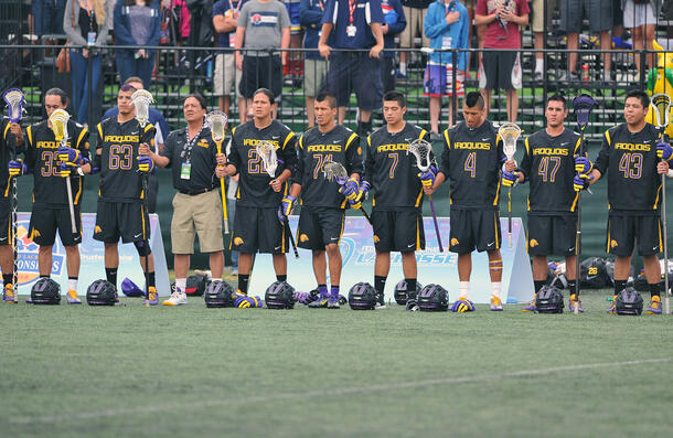 Group of players stand side-by-side, holding their lacrosse sticks.