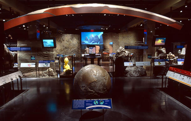 Large bronze model of planet earth is displayed in the middle of a Museum hall which contains geological specimens.