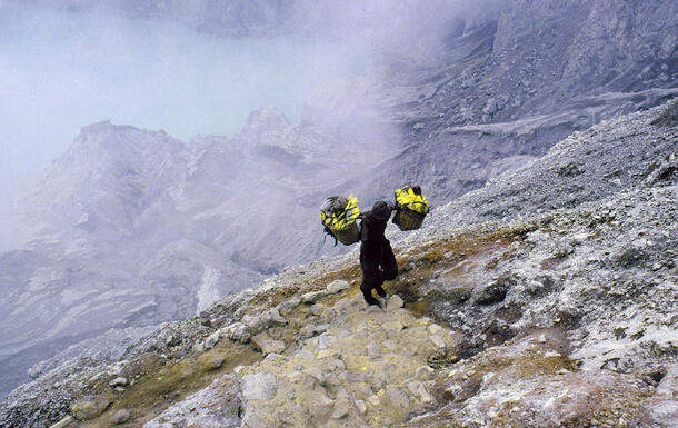 Miner carries baskets of sulfur across his shoulders as he walks up the mountain.