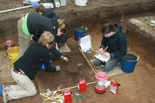 Four people at work in an excavation pit, using tools and recording information.