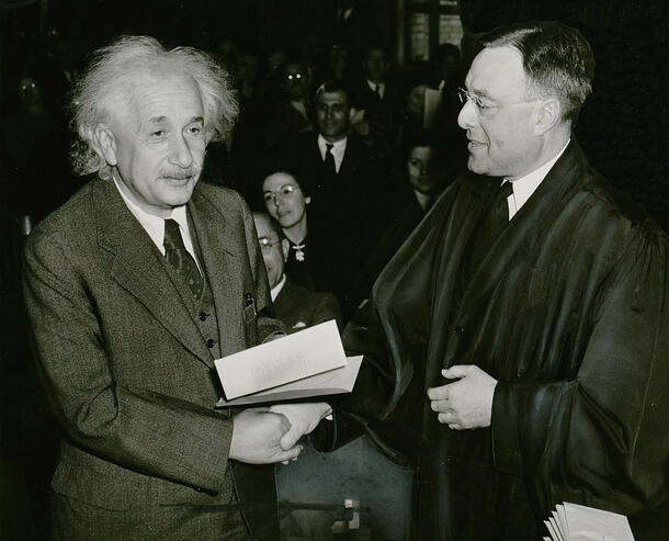 Albert Einstein holds papers and shakes the hand of a judge.