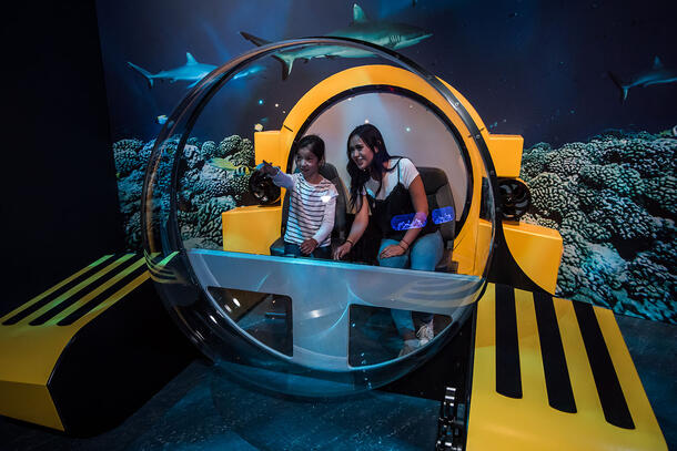Two Museum visitors sit inside the partial replica of a Triton submersible.